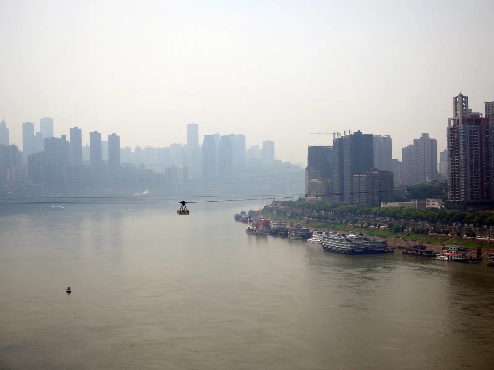 A red Yangtze River Cableway cabin crossing high above the river toward the Chongqing skyline