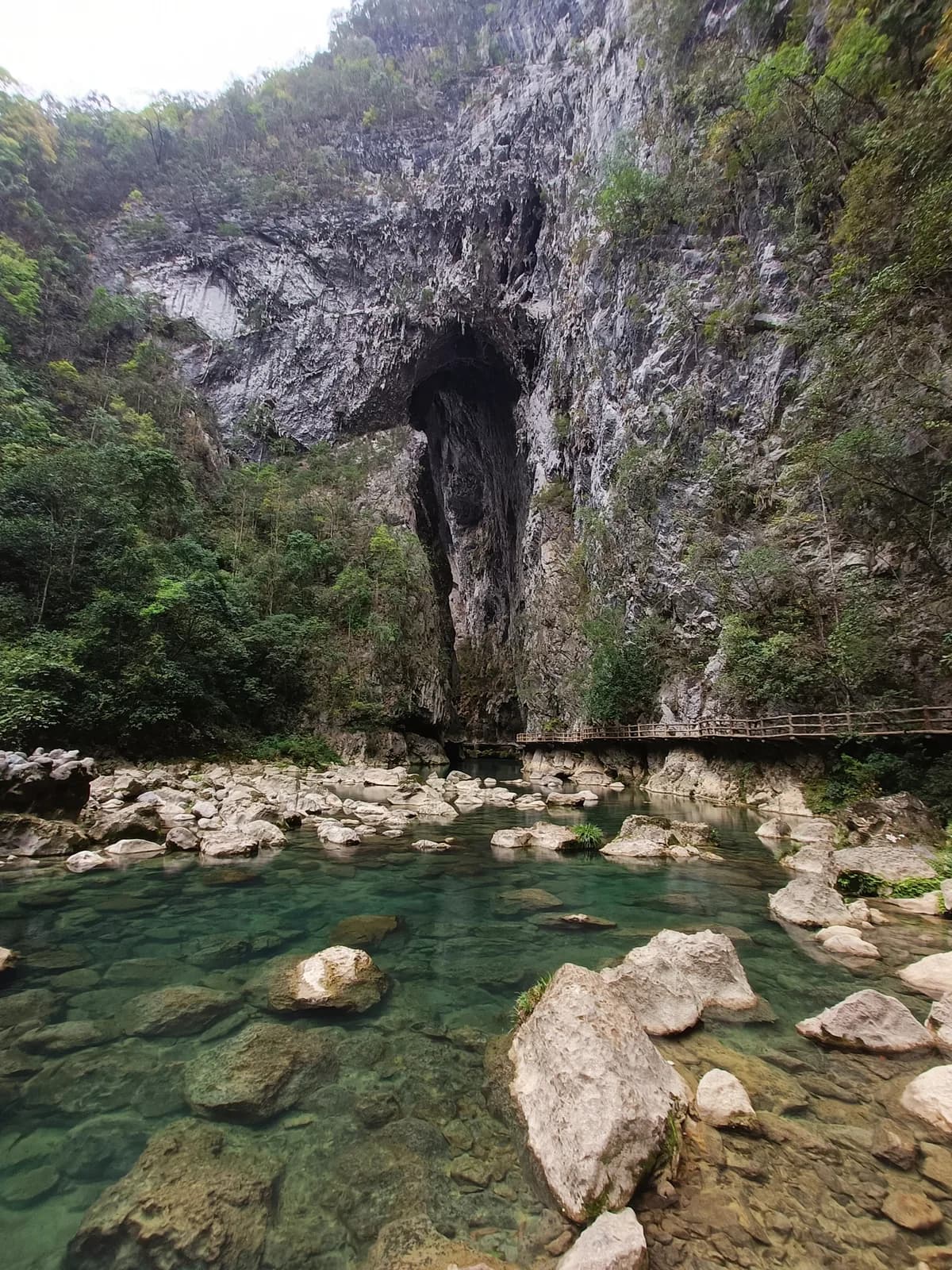 Tiansheng Bridge, a massive natural karst arch above a clear rocky river in Daqikong Scenic Area, Libo