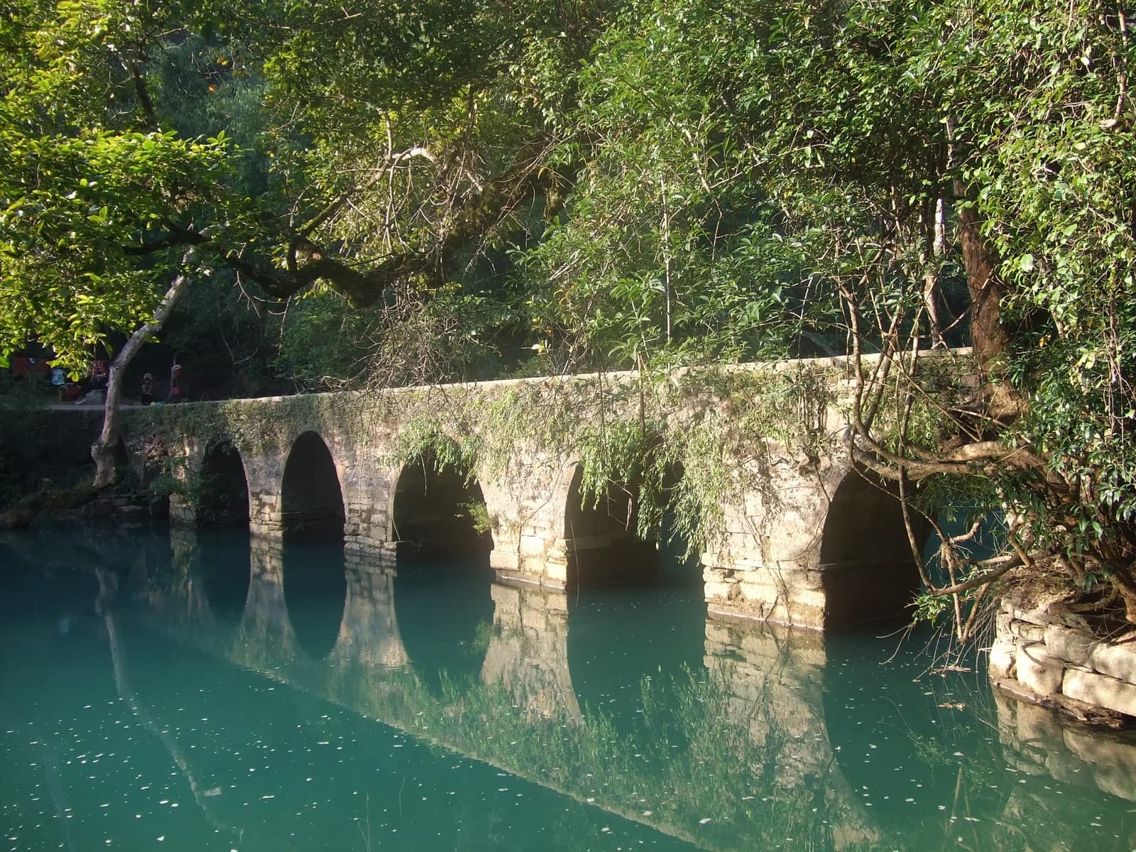 Seven-arch stone bridge of Xiaoqikong reflected in the blue-green river, draped in trees