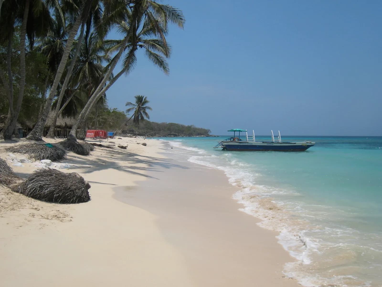 Quiet stretch of white sand at Playa Blanca with leaning palms and a single boat moored in turquoise water
