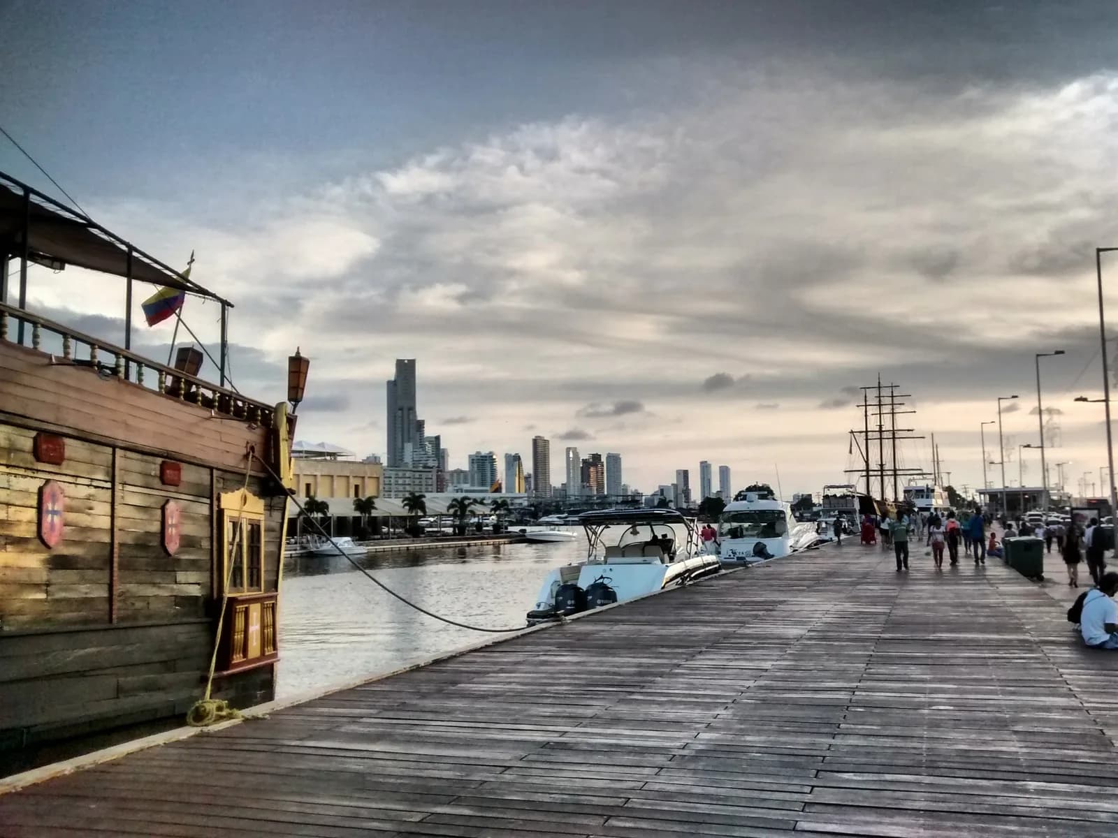 Wooden boardwalk at Muelle de los Pegasos in Cartagena with tour boats moored and the Bocagrande skyline behind