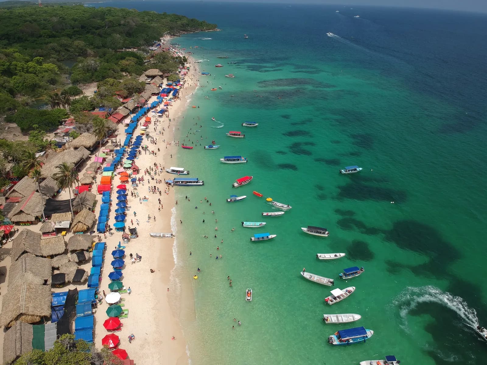 Aerial view of Playa Blanca on Isla Barú with rows of coloured umbrellas and dozens of tour boats moored off the white sand