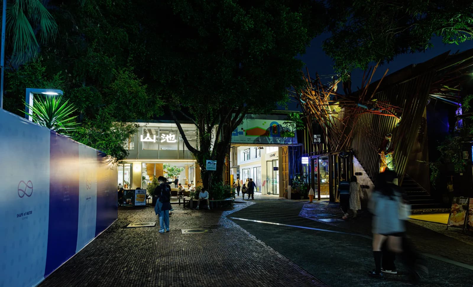 Tree-lined pedestrian lane between converted factory buildings at OCT-Loft in Shenzhen