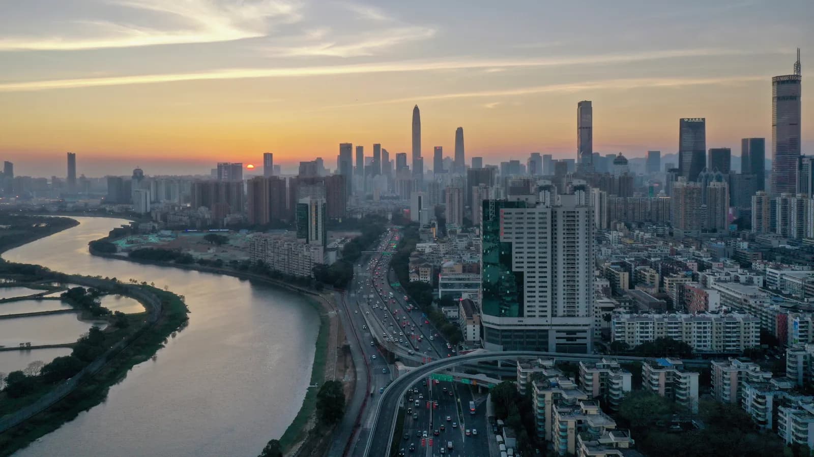 The western Shenzhen skyline at dusk with towers lit against an orange sky