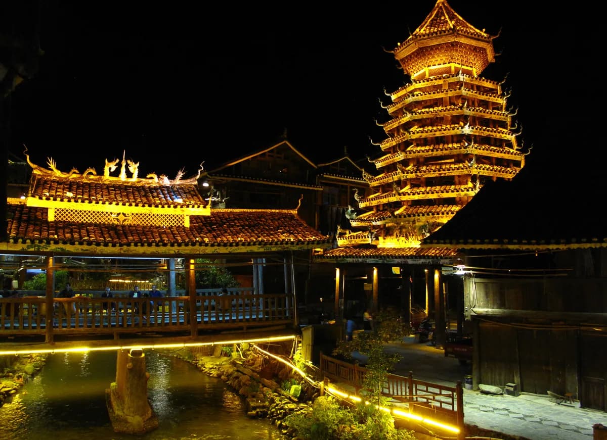 A drum tower and covered bridge in Zhaoxing Dong village illuminated with warm golden light at night